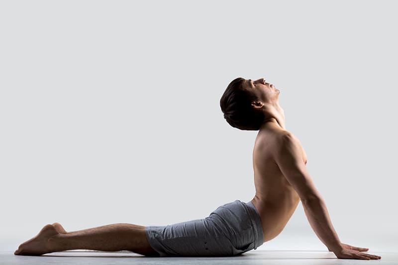 Người đang thực hiện tư thế uốn cong lưng trong yoga trên nền trắng, mặc quần ngắn màu xám.
